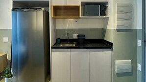 Kompakti keittiö, jossa on ruostumattomasta teräksestä valmistettu jääkaappi, mikroaaltouuni ja pesuallas.