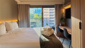 A modern hotel room with a large bed, a desk with a chair, a potted plant, and a view of the city through a balcony. - ON MELO ALVES (São Paulo)