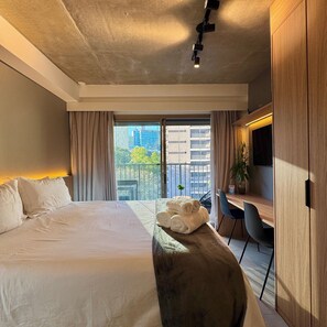 A modern hotel room with a large bed, a desk with a chair, a potted plant, and a view of the city through a balcony. - ON MELO ALVES (São Paulo)