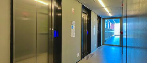 A corridor with elevators, a blue exit sign, and a fire alarm.