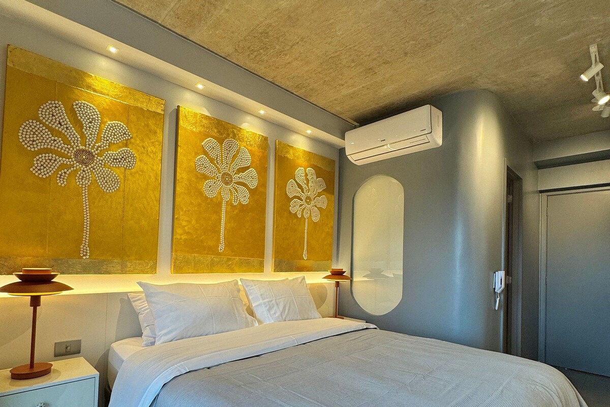 A modern bedroom with a large bed, bedside tables, a wall-mounted air conditioner, and decorative wall art.