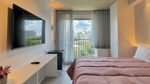 Un dormitorio moderno con cama, televisor, escritorio y ventana con cortinas.