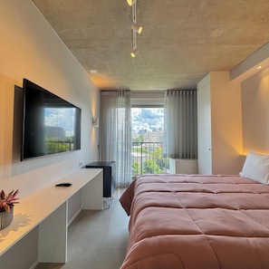 Una camera da letto moderna con un letto, una TV, una scrivania e una finestra con tende.
