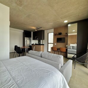 A modern hotel room with a large bed, a sofa, a dining area with chairs, a kitchen, and a TV mounted on the wall. - ON MELO ALVES (São Paulo)