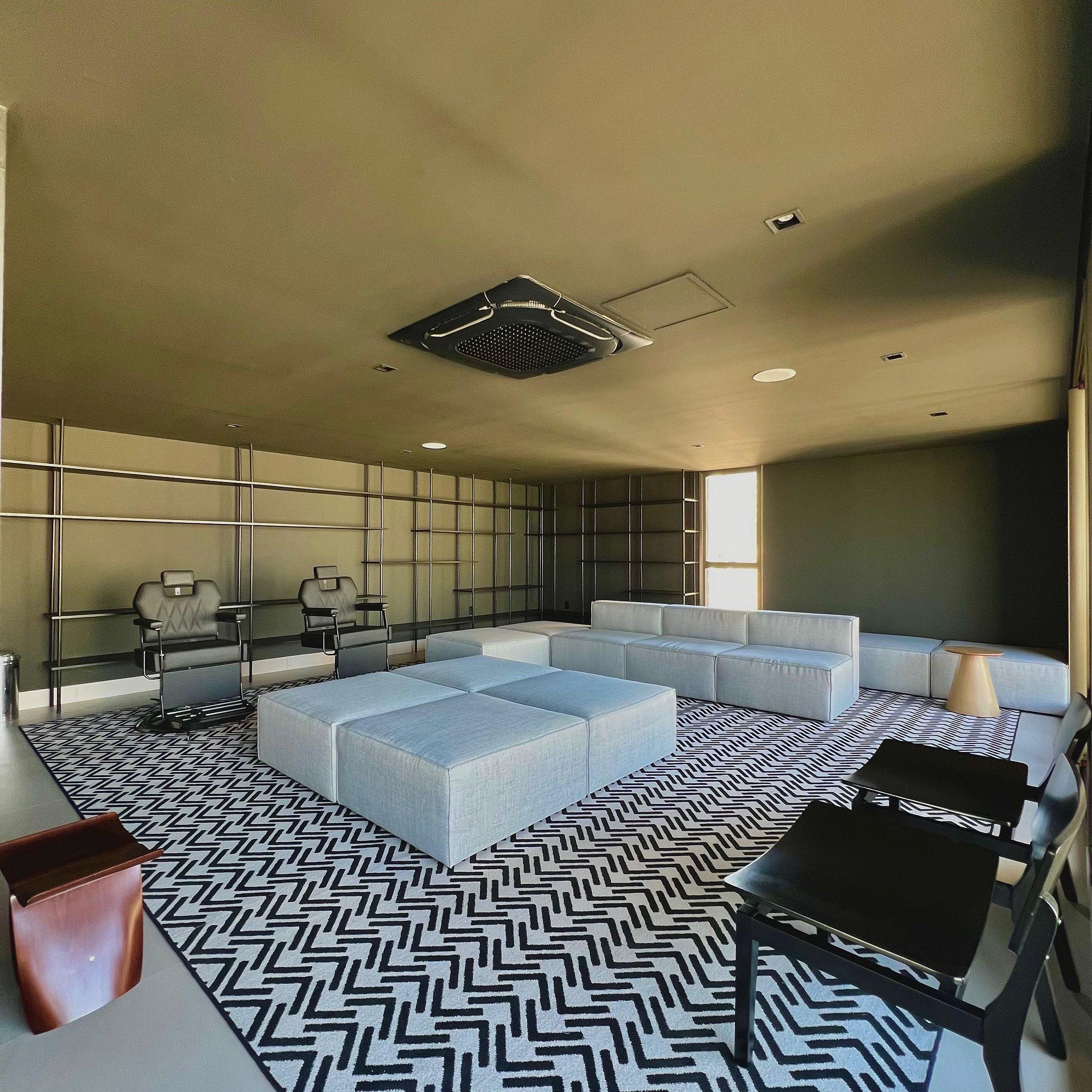 Uma sala de estar moderna com um sofá modular, um tapete estampado e um respiradouro no teto.