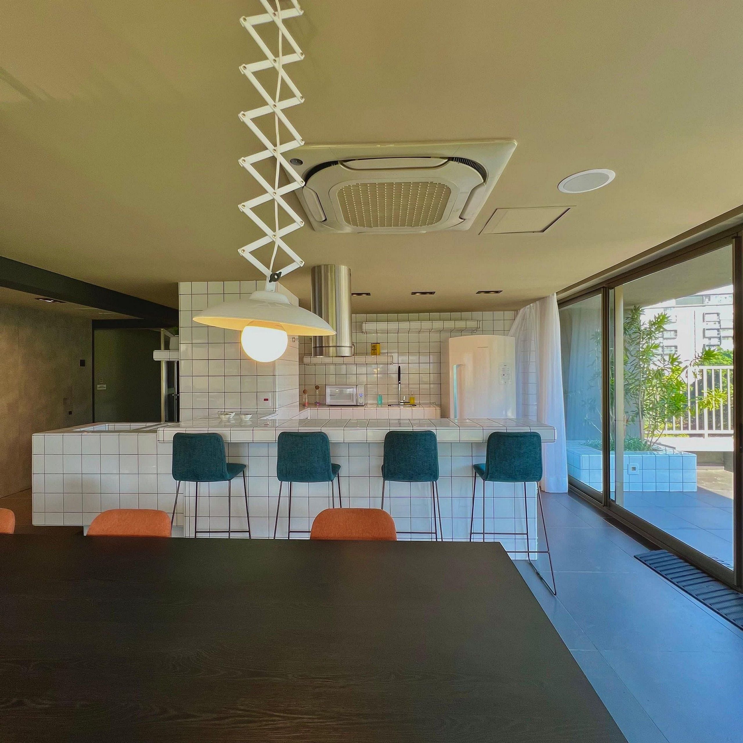 A modern kitchen with white tiles, a central island, bar stools, and a dining table.