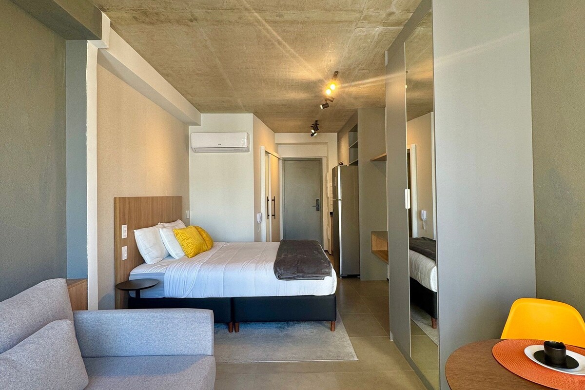 A modern hotel room with a bed, a sofa, a dining table, and a mirror.