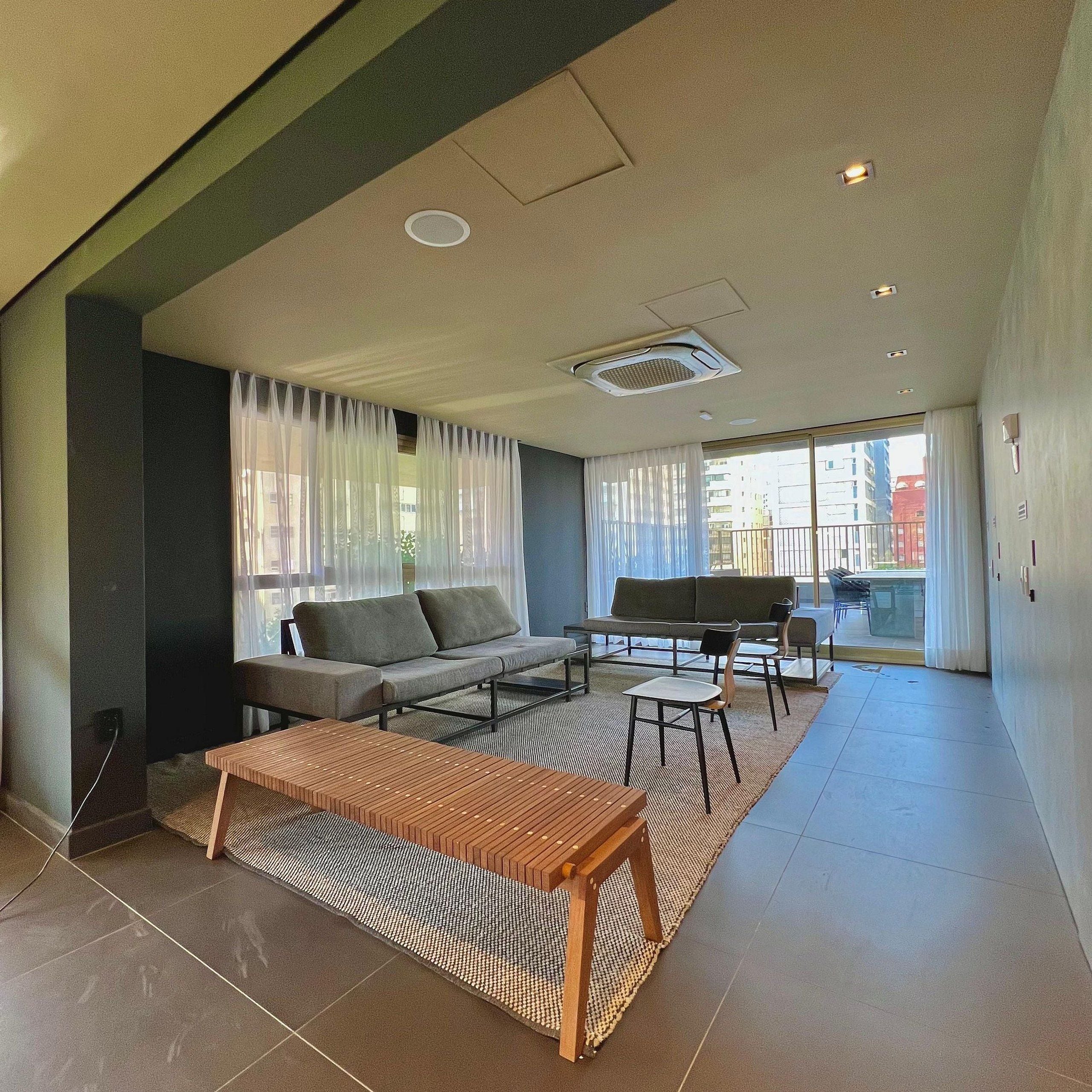 Un salon moderne avec un canapé, une table basse et des fauteuils, une grande fenêtre avec des rideaux et une vue sur les bâtiments à l’extérieur.
