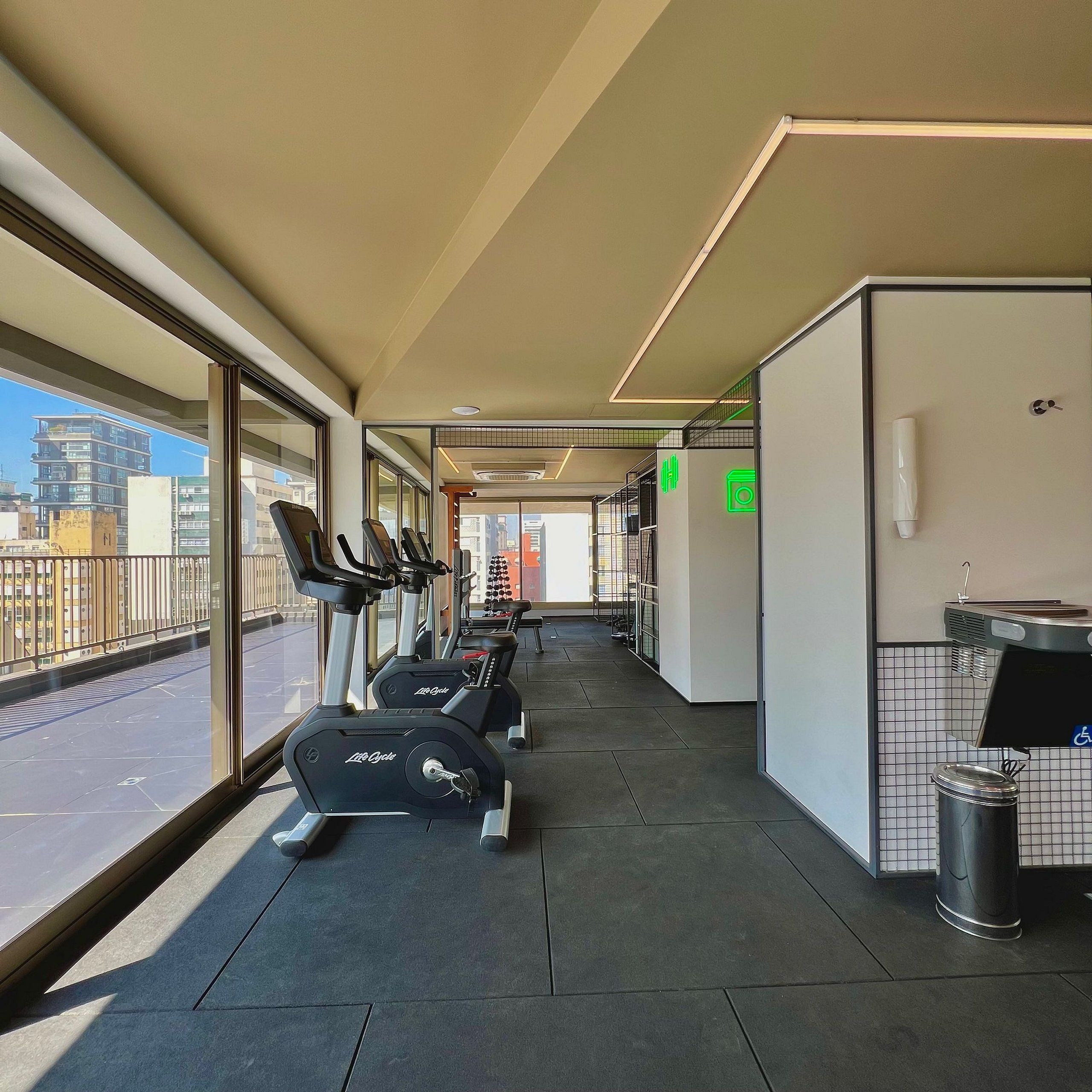 Un gimnasio con cintas de correr, un bote de basura y vistas a la ciudad.