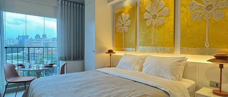 A modern hotel room with a large bed, a city view, and decorative wall art.
