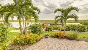 Un jardín ajardinado con palmeras, un sendero pavimentado y vista a un cuerpo de agua.