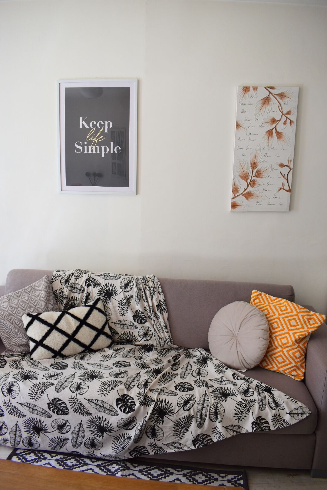 Un salon avec un canapé agrémenté d’une couverture à motifs de feuilles, une citation encadrée au mur et une estampe décorative représentant des feuilles.