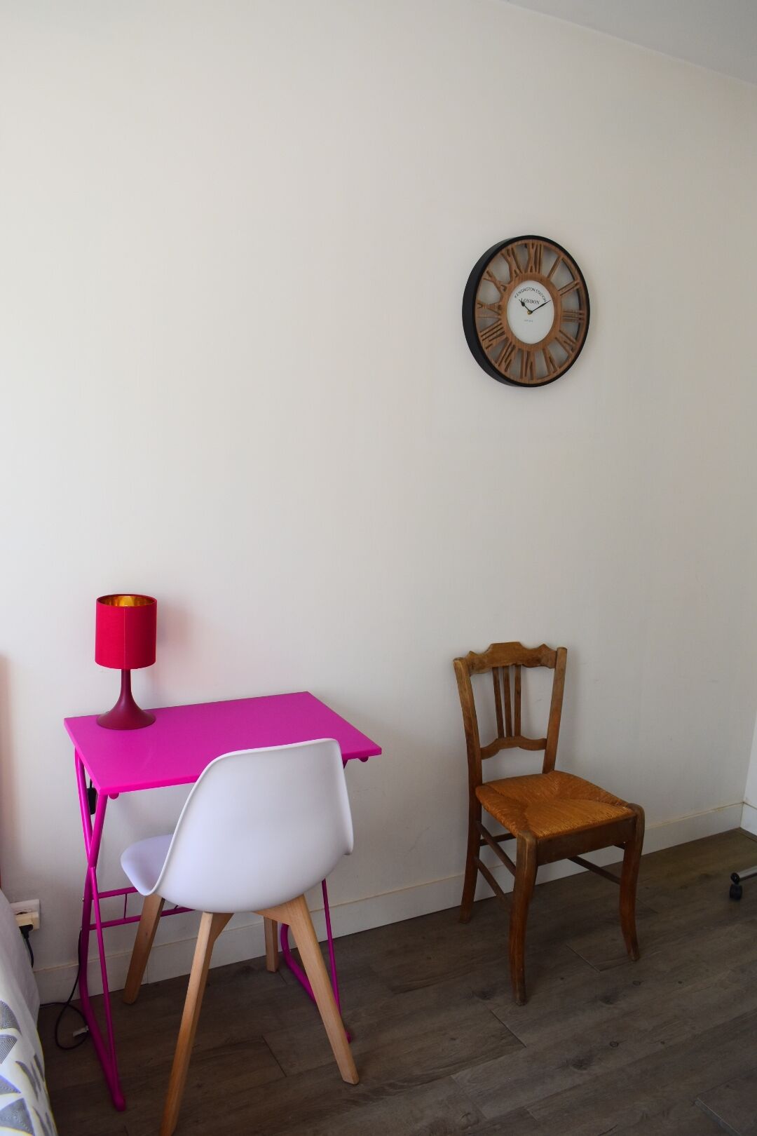 Et værelse med et pink bord, en hvid stol, en træstol og et vægur.