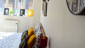 Une pièce comprenant un lit, une table, une horloge et une fenêtre donnant sur des immeubles.
