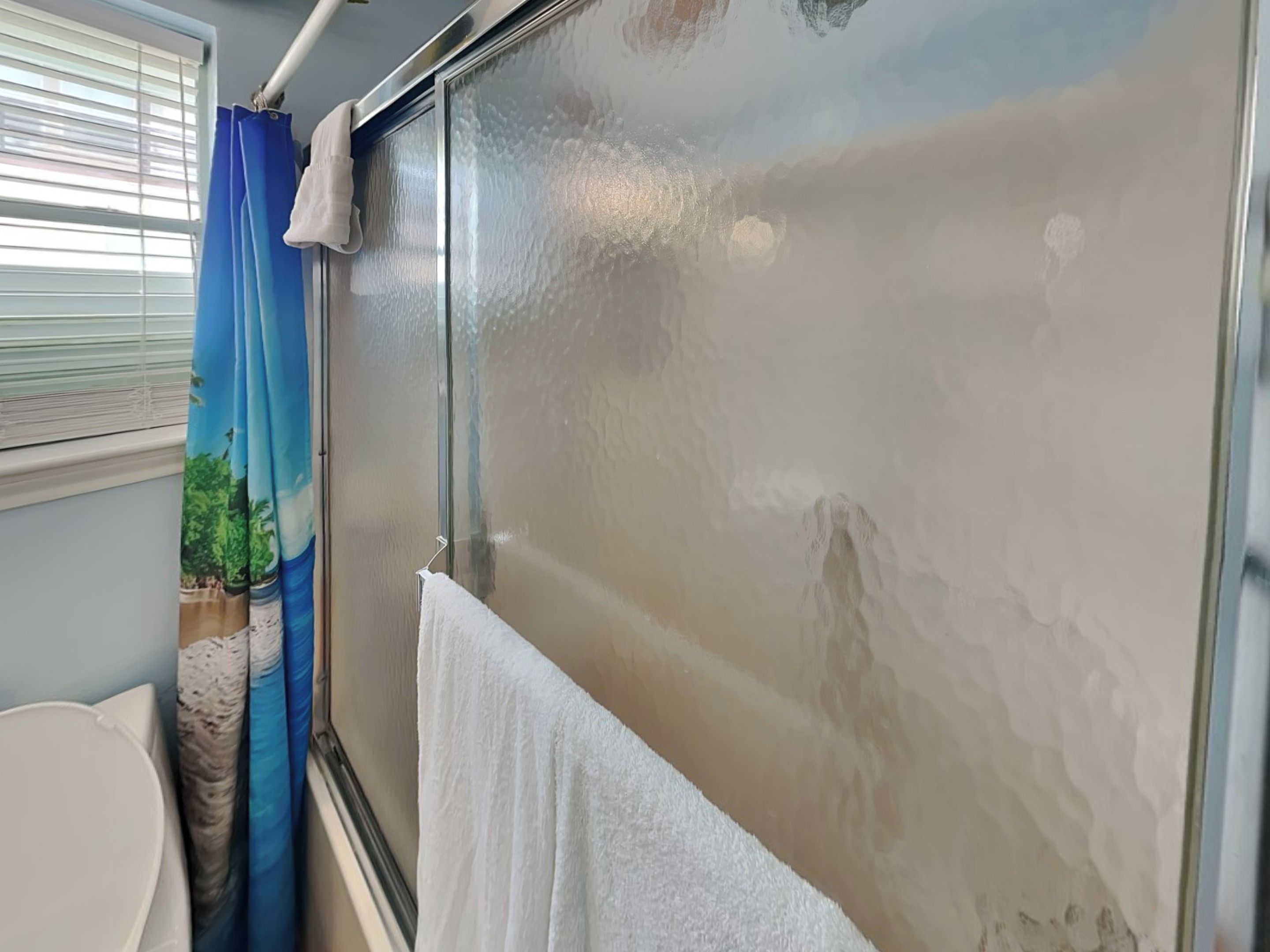 A bathroom with a bathtub, a window with a view of greenery, and a towel hanging on the wall.