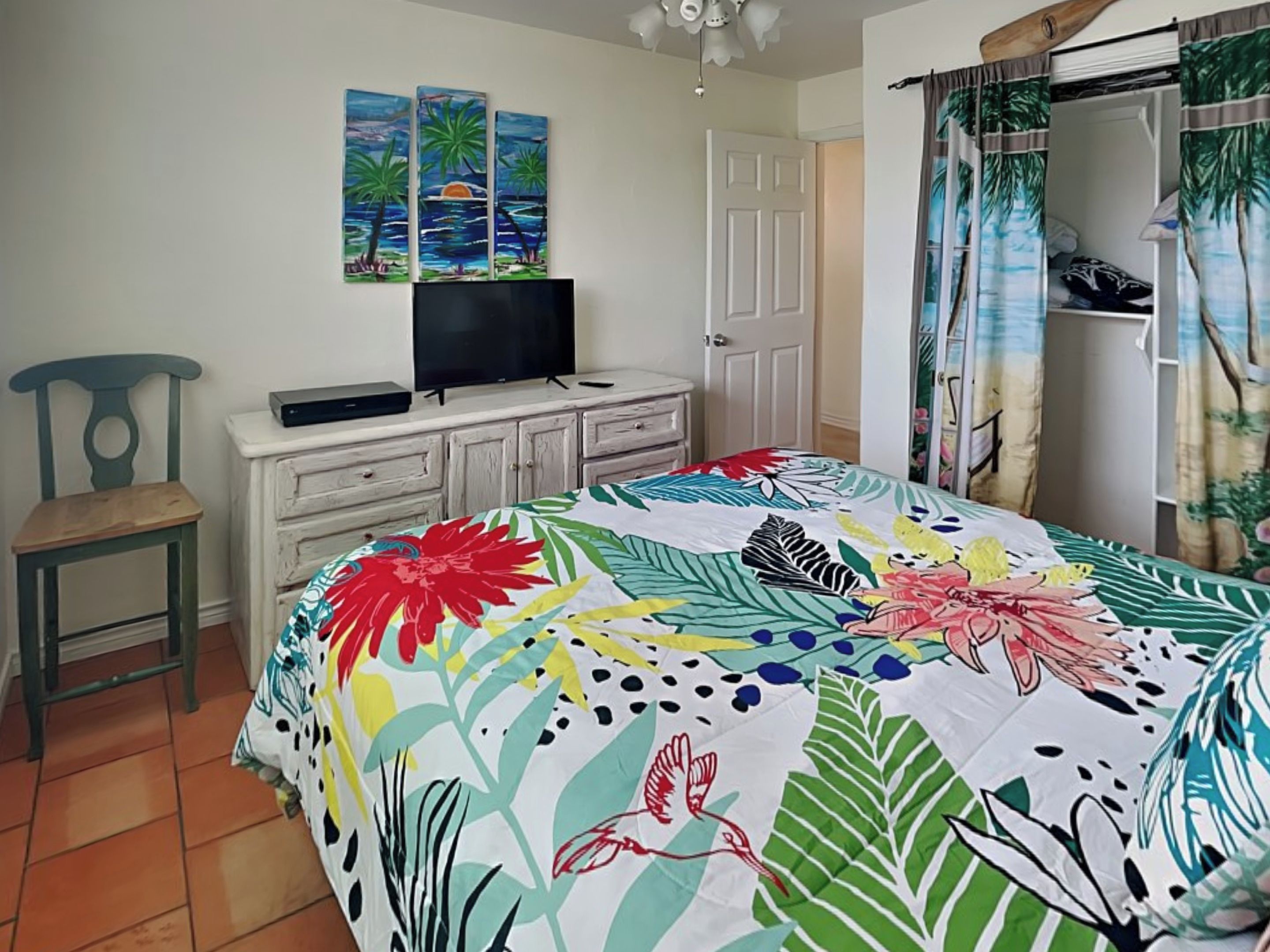A bedroom with a bed, a television on a dresser, a chair, and a door.