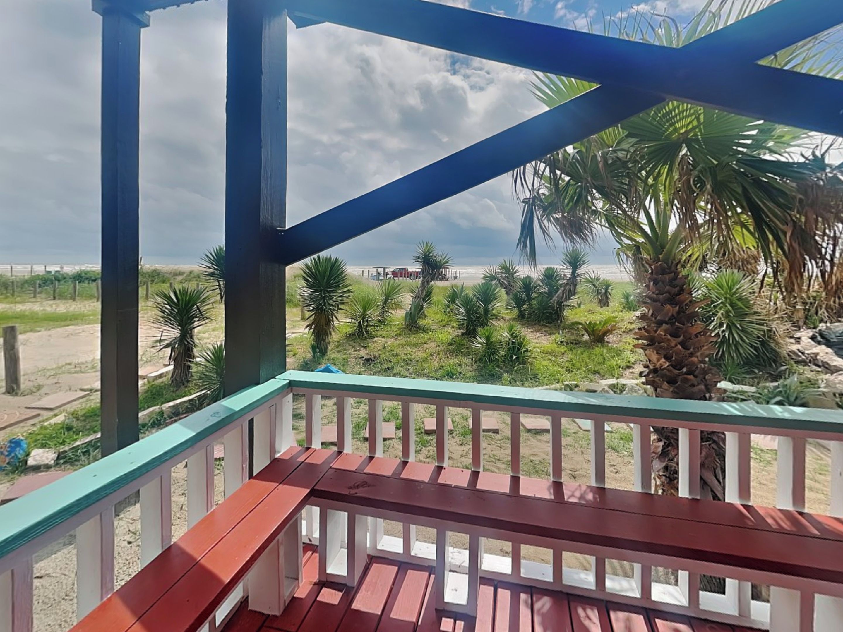 A wooden deck with a view of a beach and palm trees.