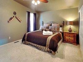 A bedroom with a bed, a nightstand, a lamp, a window with curtains, and a ceiling fan.