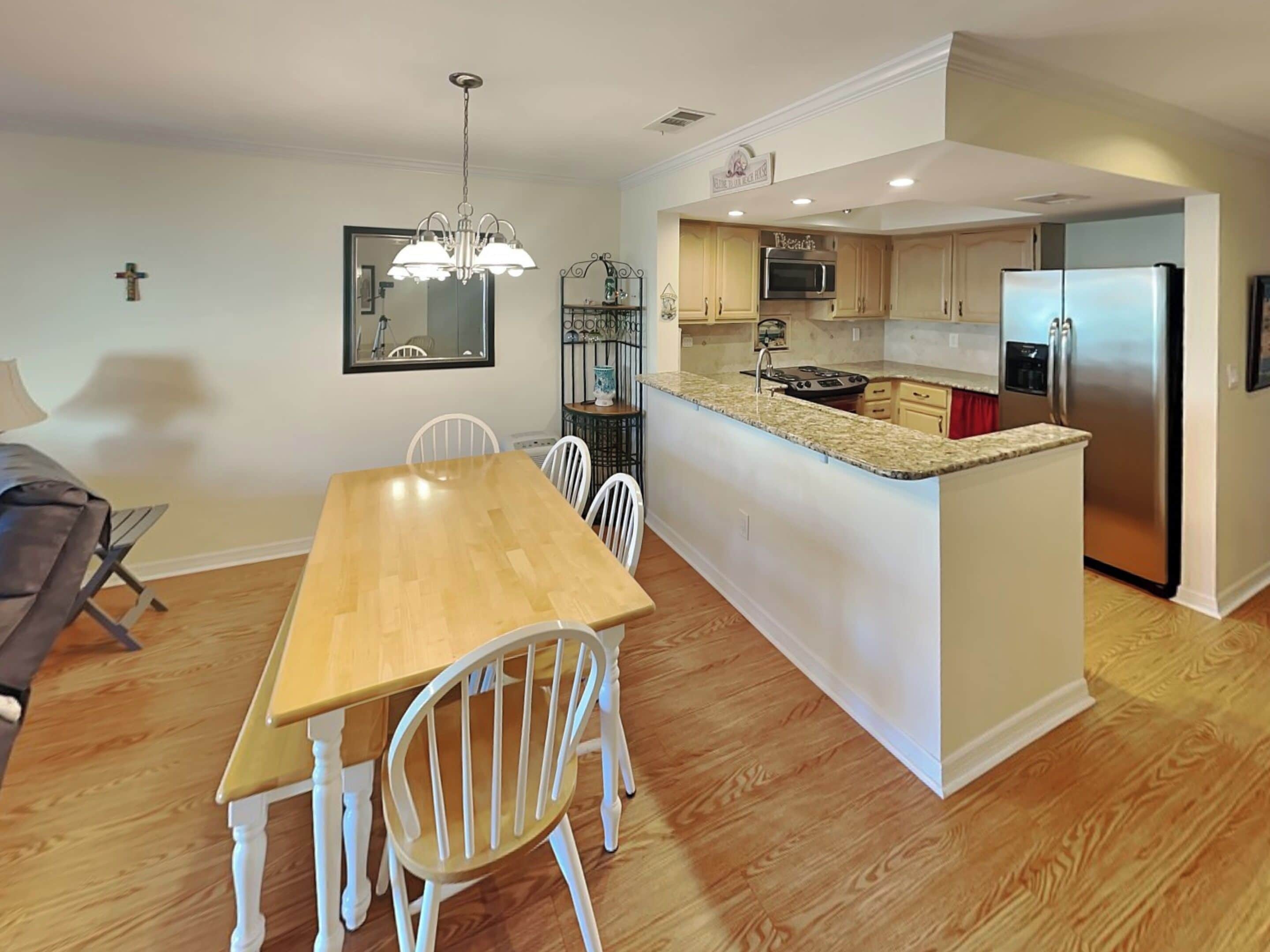 Una cocina moderna con una isla central, mesa de comedor de madera, sillas blancas y una araña.