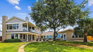 A two-story house with a covered porch, a large tree in the front yard, and a well-maintained lawn. - Amazing Bay by Ryson Vacation Rentals (Galveston)