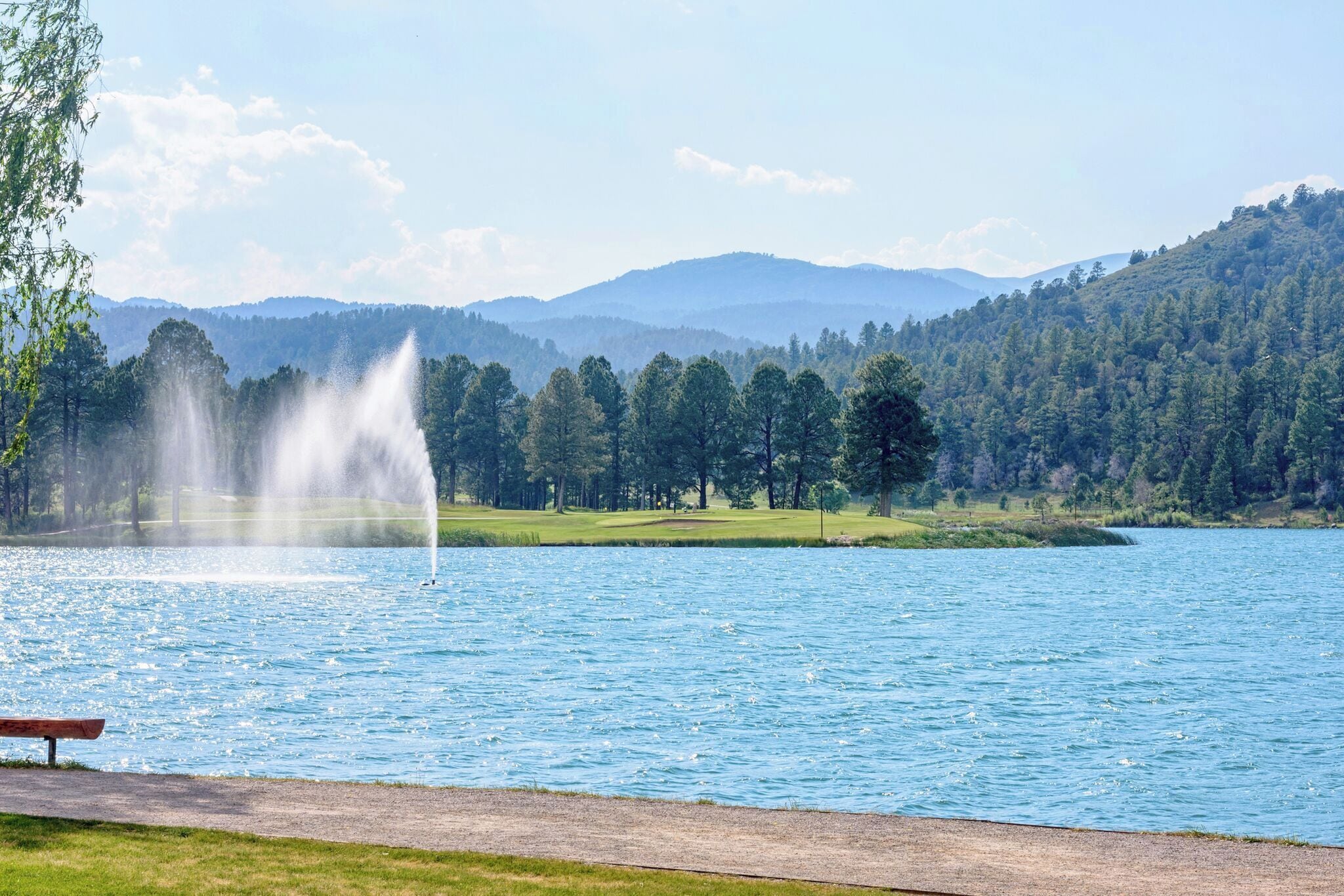 A lake with a fountain, surrounded by trees and hills.