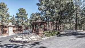 A gazebo in a wooded area with a paved road and buildings in the background. - Pinon Park C11 by Ruidoso Vacation Rentals (Ruidoso)