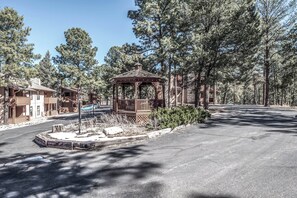 A gazebo in a wooded area with a paved road and buildings in the background. - Pinon Park C11 by Ruidoso Vacation Rentals (Ruidoso)