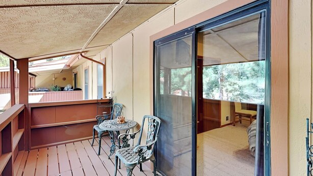 A wooden deck with a sliding glass door leading to a bedroom. There are two chairs and a small table on the deck. - Pinon Park C11 by Ruidoso Vacation Rentals (Ruidoso)