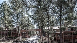 A gated entrance to Pinon Park condominiums with a stone pathway leading through a forested area. - Pinon Park C11 by Ruidoso Vacation Rentals (Ruidoso)