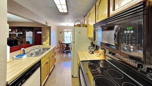 A kitchen with a microwave, stove, and sink. There is a dining area with a table and chairs. - Pinon Park C11 by Ruidoso Vacation Rentals (Ruidoso)