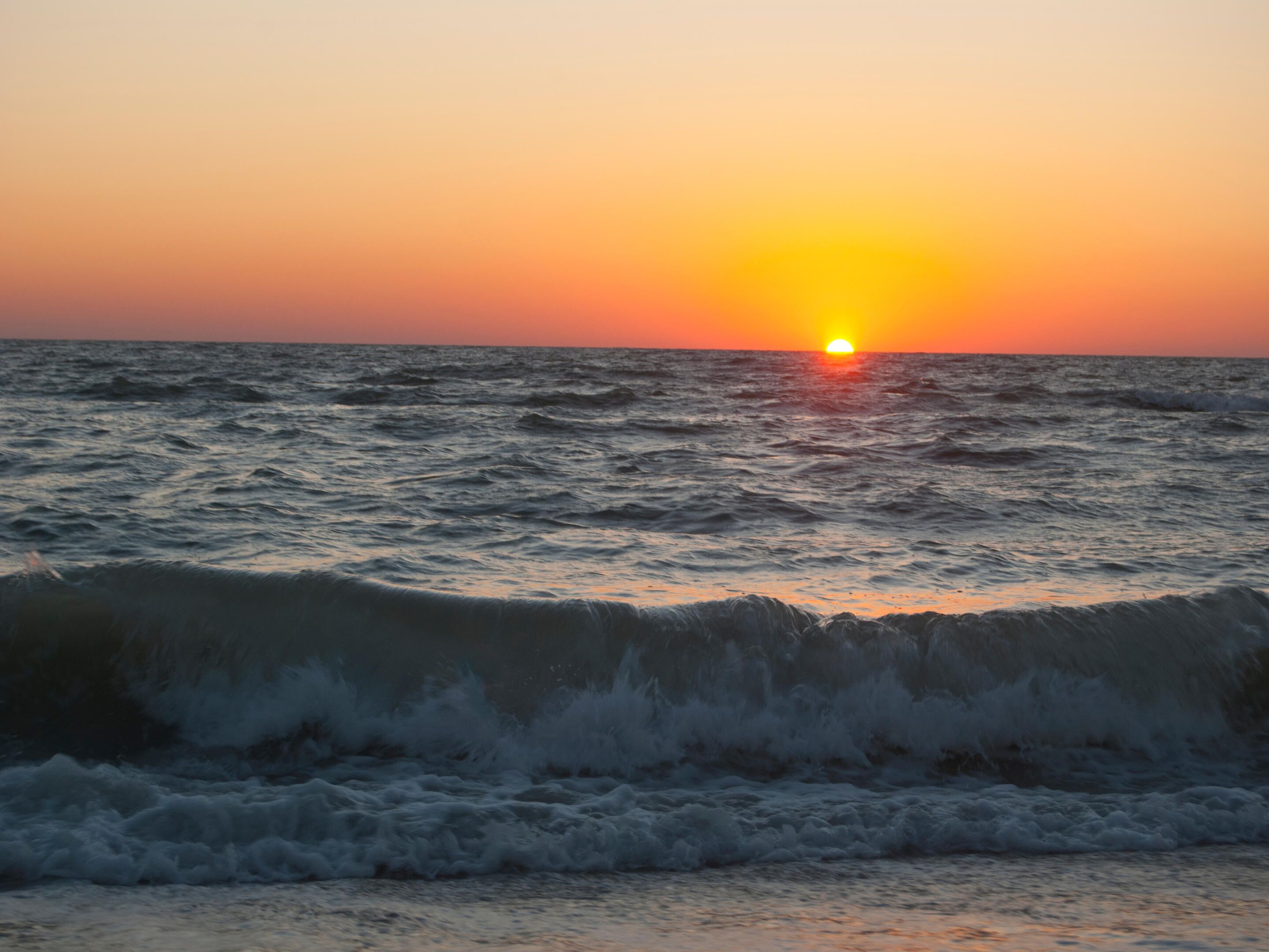 A sunset over the ocean with waves crashing onto the shore.