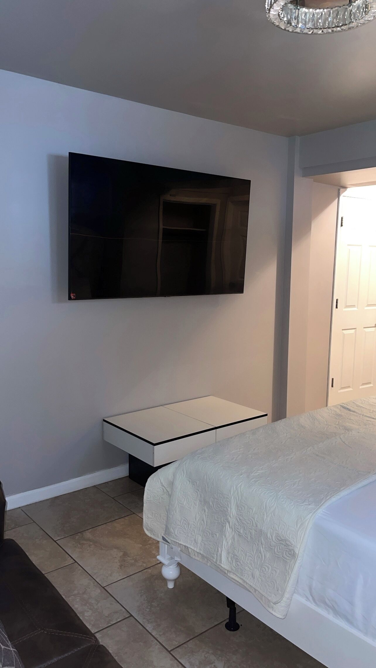 A bedroom with a bed, a bedside table, a TV mounted on the wall, and a door.