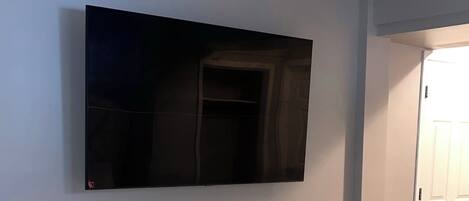 A bedroom with a bed, a bedside table, a TV mounted on the wall, and a door.