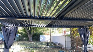 A covered outdoor area with a metal roof, a picnic table, and a fence. - Cozy 1-bedroom Apt with WiFi and beautiful backyard view (Belleville)