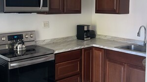 A modern kitchen with dark wooden cabinets, stainless steel appliances, a marble countertop, and a tiled floor. - Cozy 1-bedroom Apt with WiFi and beautiful backyard view (Belleville)
