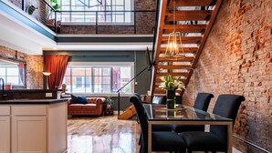 Ein geräumiges Loft mit hoher Decke, freiliegenden Backsteinwänden und einer Holztreppe.