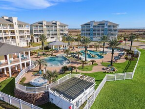 A resort with multiple buildings, a central swimming pool, and surrounding palm trees. - Beachside Blue Sailfish by Ryson Vacation Rentals (Galveston)
