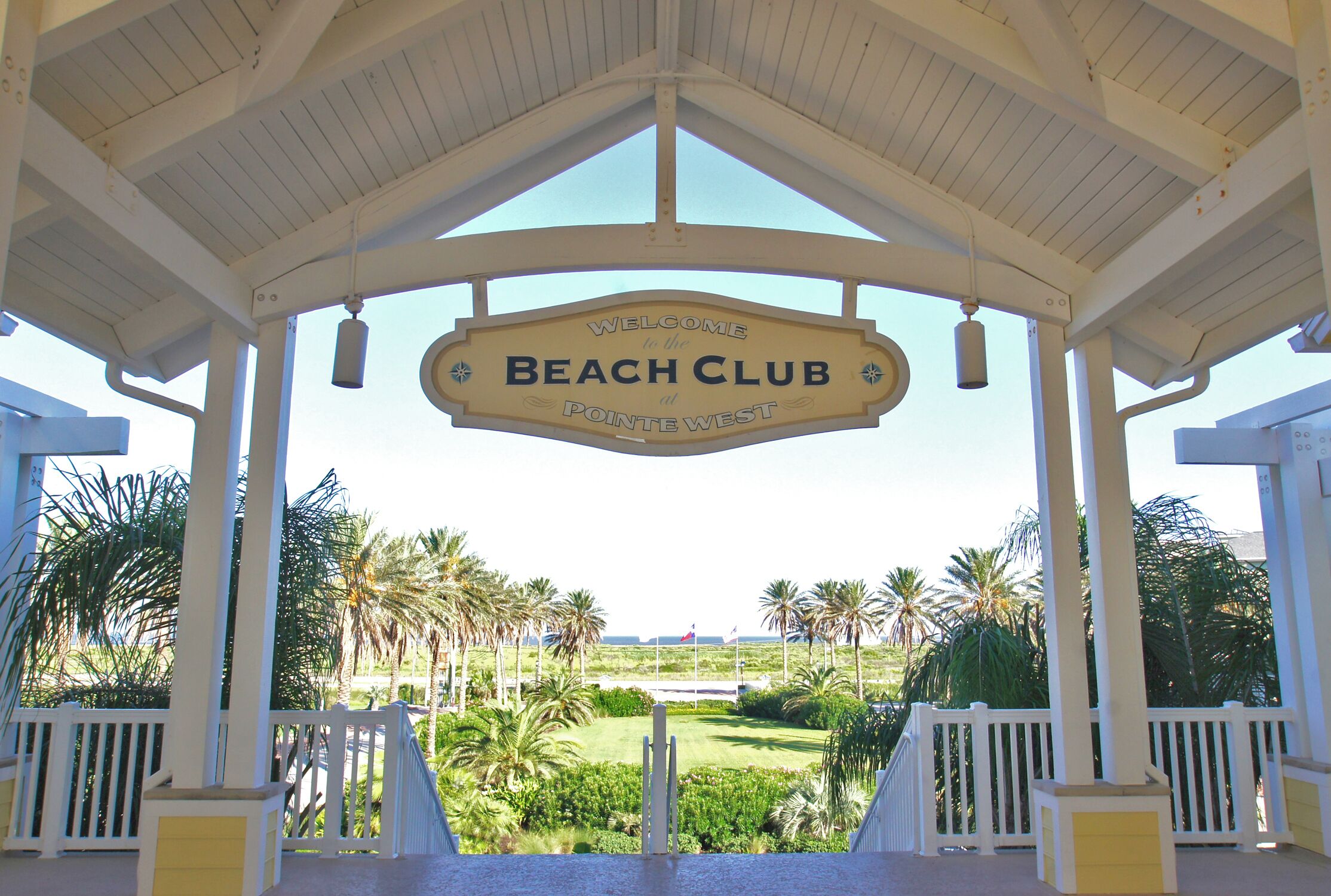 A beach club sign with a view of palm trees and a golf course.