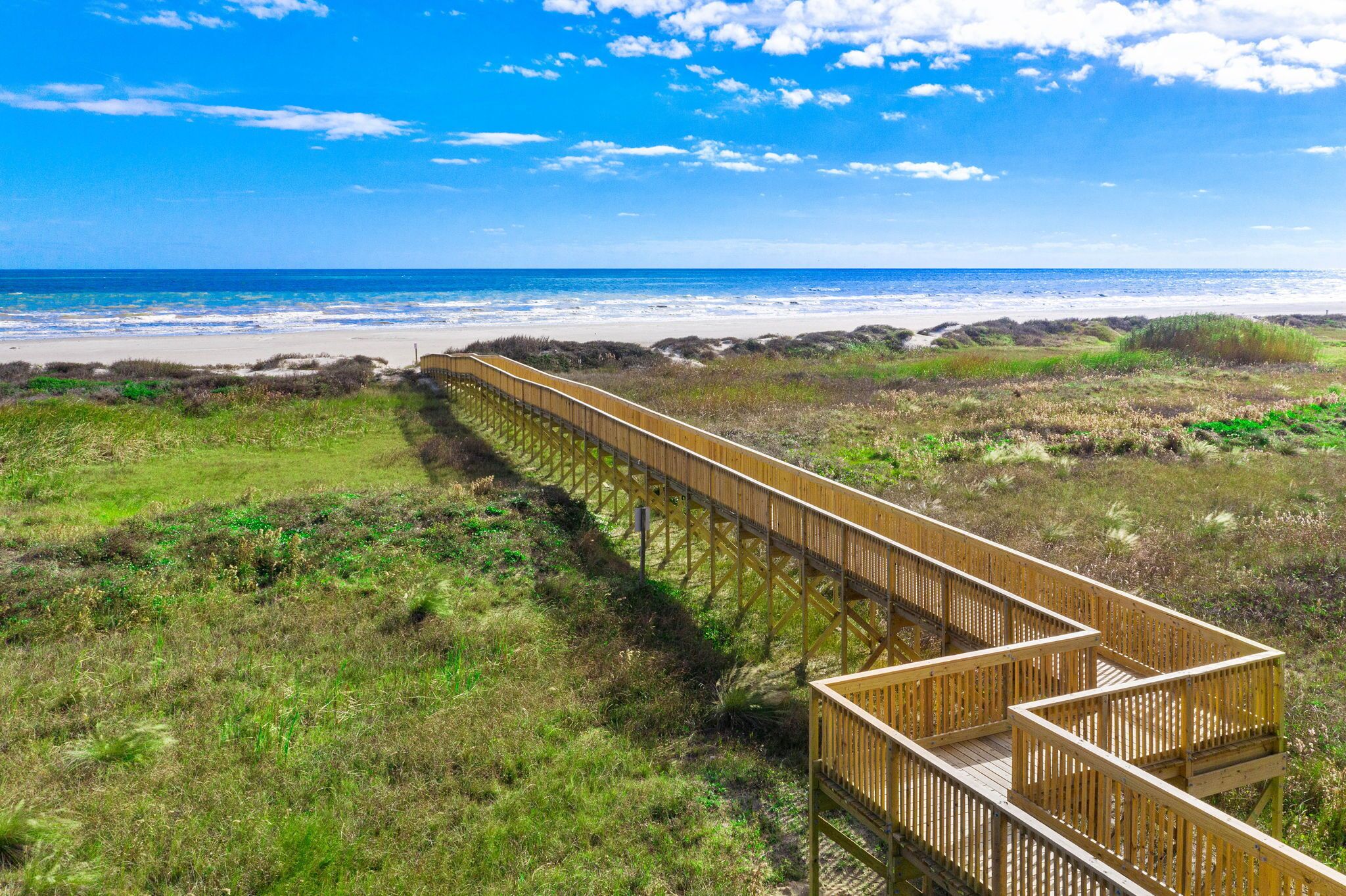 Une promenade en bois qui mène à une plage offrant une vue dégagée sur l’océan.