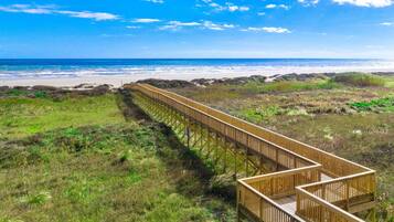 Une promenade en bois qui mène à une plage offrant une vue dégagée sur l’océan.