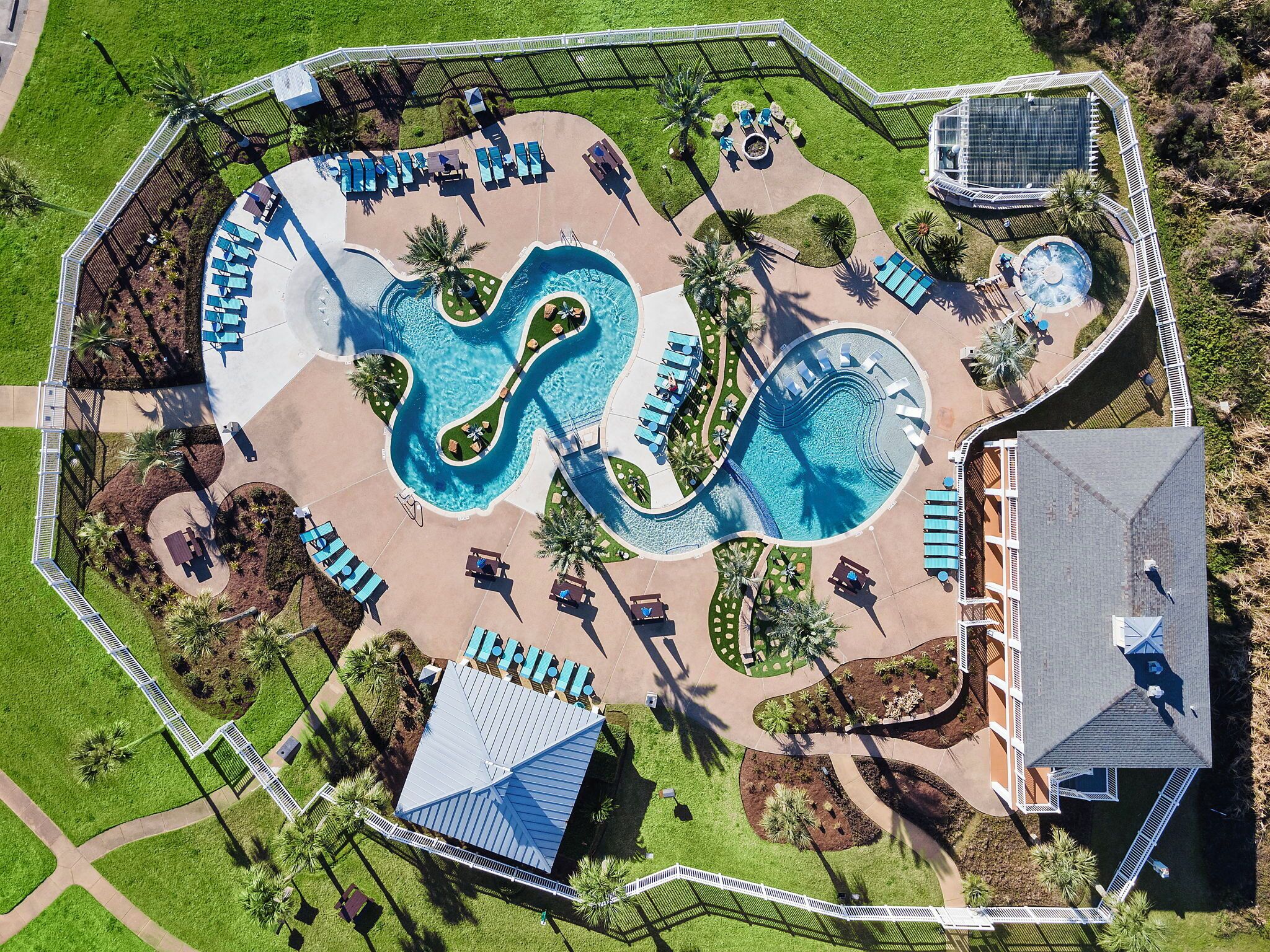 Vue aérienne d’un complexe hôtelier doté d’une grande piscine, de chaises longues et d’un petit bâtiment.