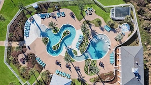 Ett flygbildsfoto av ett semesterområde med en stor pool, solstolar och en liten byggnad.