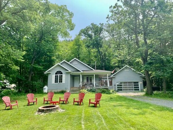 A two-story house with a porch, a garage, and a fire pit with chairs. - Forest Guest Suite Near Picton Centre (Pet-Friendly &Hot Tub &Park Pass)
(Prince Edward)
