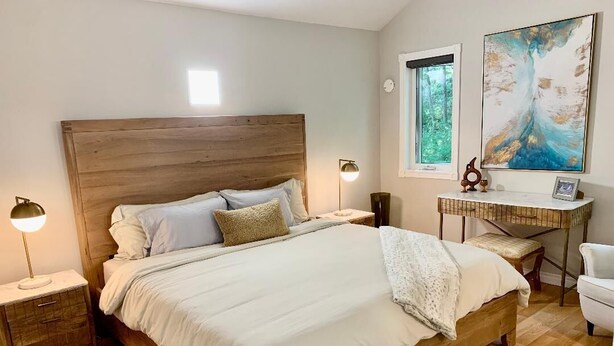 Une chambre à coucher avec un lit en bois, des tables de chevet, un bureau et une fenêtre donnant sur un paysage verdoyant.