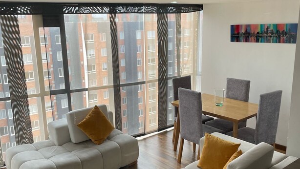 Ein modernes Wohnzimmer mit einer Sofagarnitur, einem Esstisch mit Stühlen und einem großen Fenster mit Blick auf die Stadt.