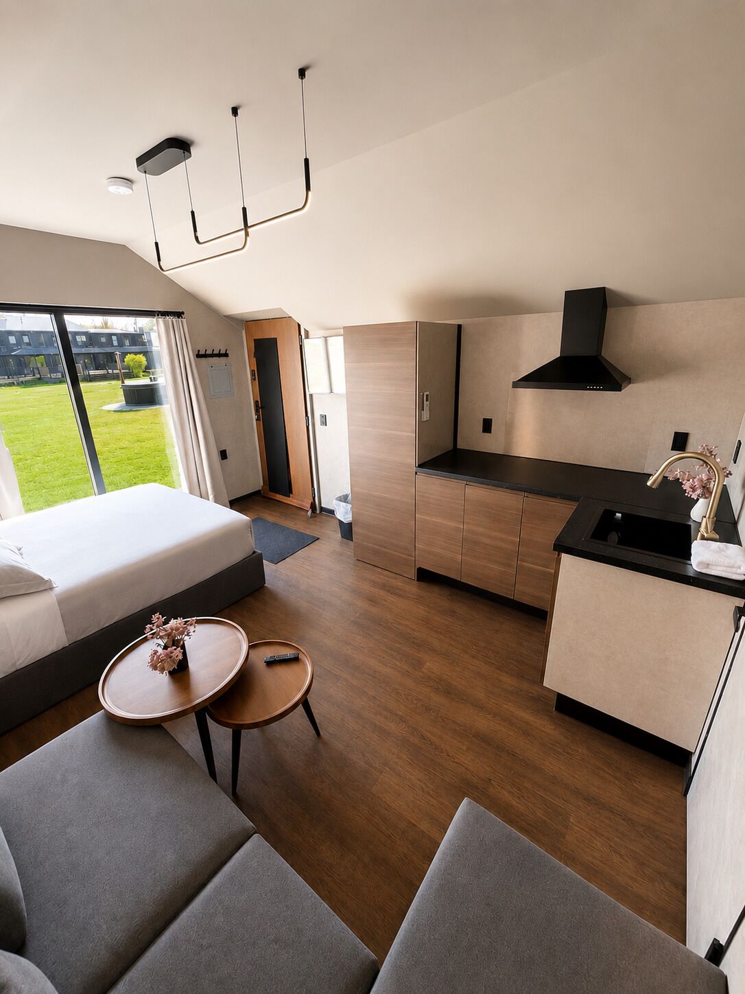 Een moderne hotelkamer met een bed, een bank, een klein rond tafeltje, een kitchenette en uitzicht op het landschap.