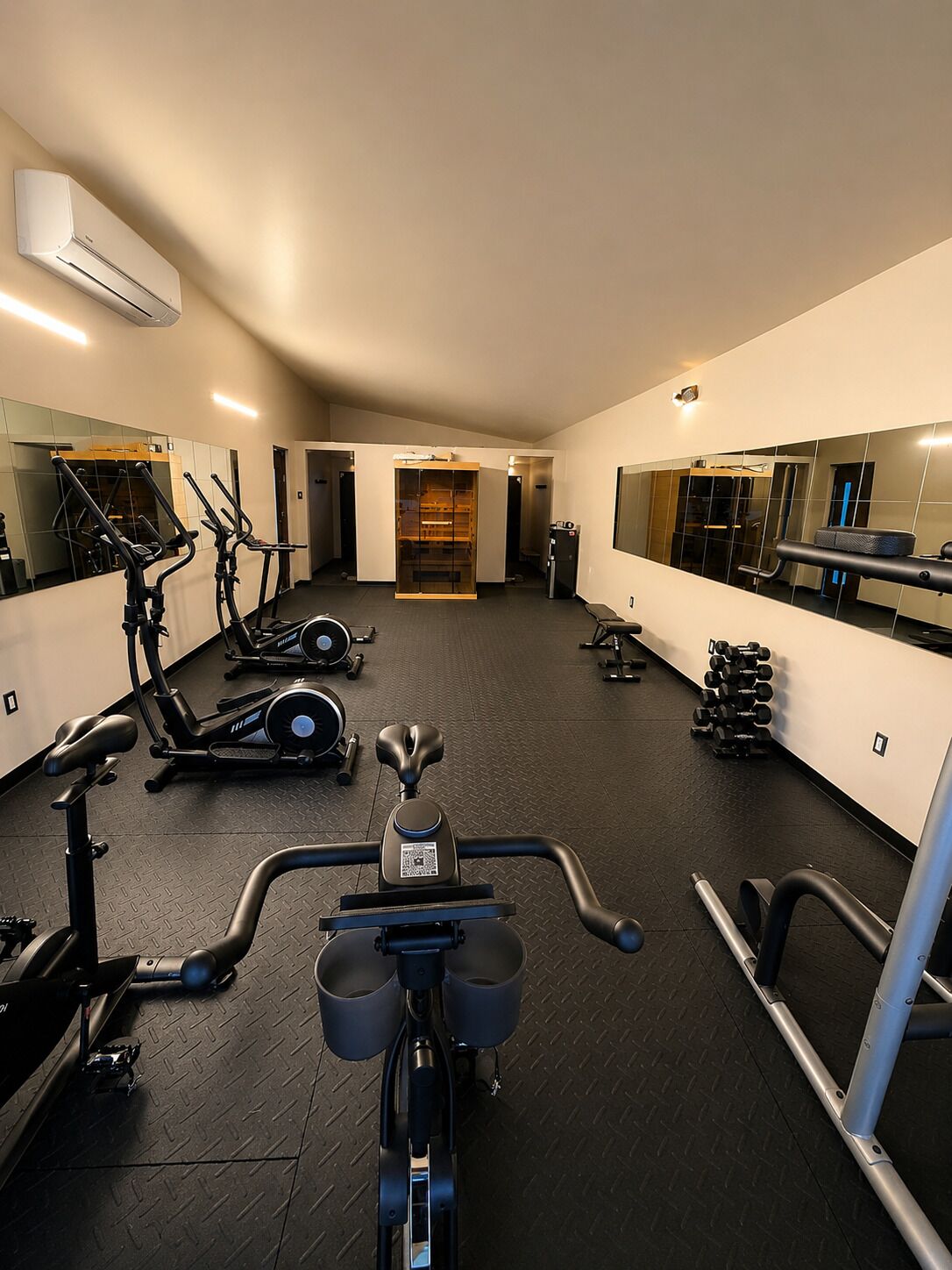 A gym with exercise equipment, a mirrored wall, and a black rubber floor.