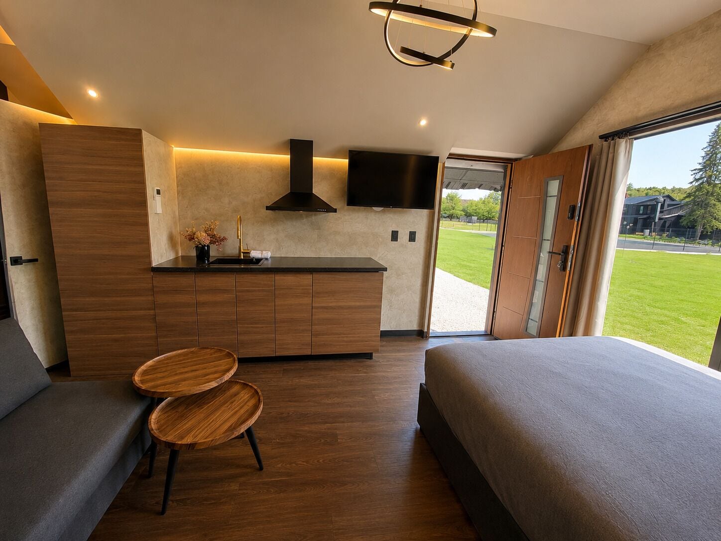 Un dormitorio moderno con una cama grande, una mesita de madera, una cocina integrada y un ventanal amplio.