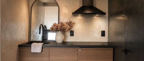 A modern kitchen with wooden cabinets, a black range hood, a mirror, and a vase with dried flowers.