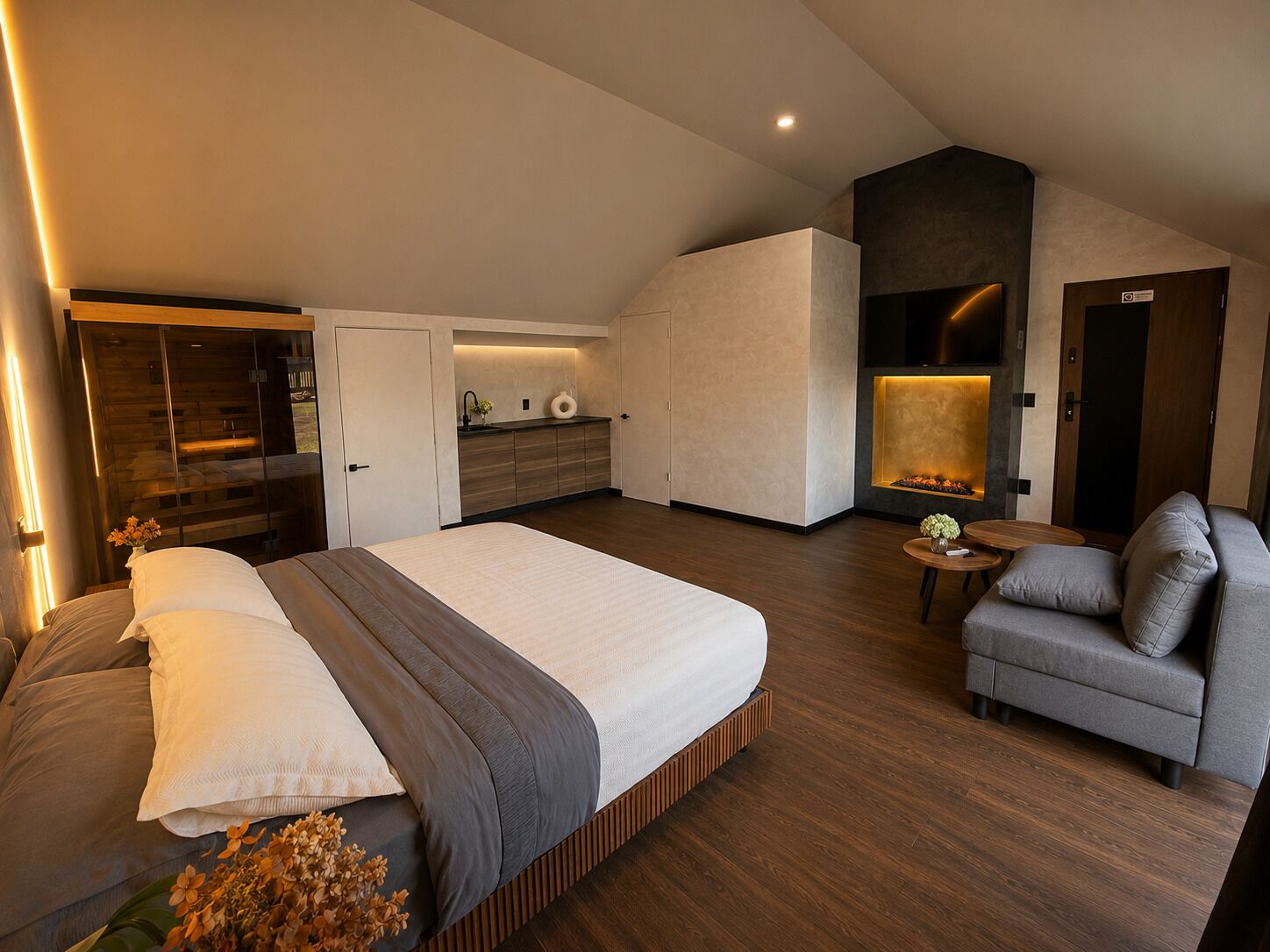 A modern bedroom with a large bed, a sofa, a small table, and a fireplace.